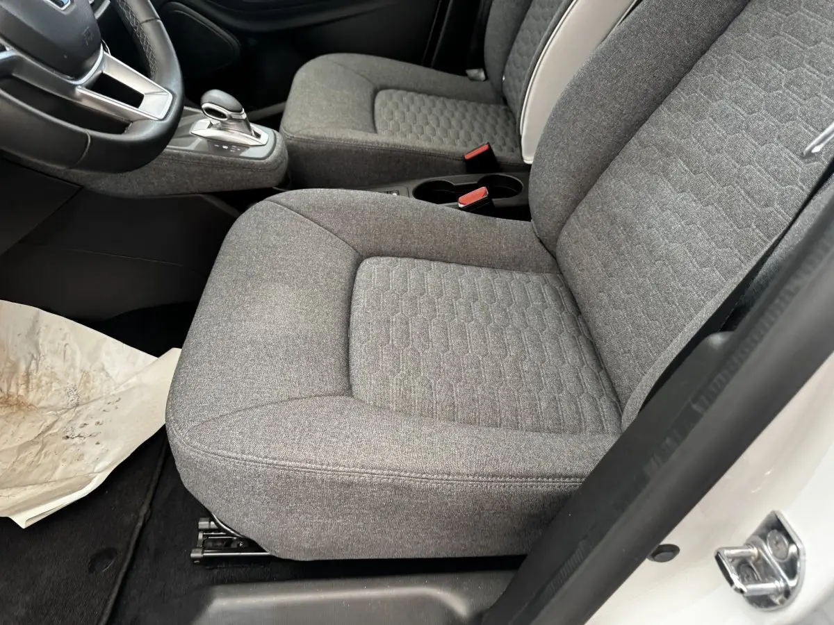 Vue intérieure côté conducteur de la Renault ZOE blanche, sièges avant gris tissu avec console centrale et levier de vitesse.