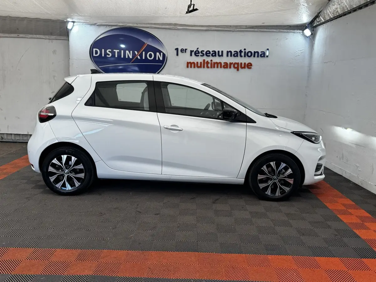Profil côté gauche d'une Renault ZOE blanche Iconic R135 2022, avec jantes alliage et rétroviseurs noirs.