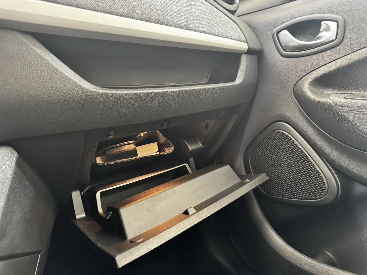Vue intérieure côté passager de la boîte à gants ouverte de la Renault ZOE blanche, montrant le rangement et la porte.