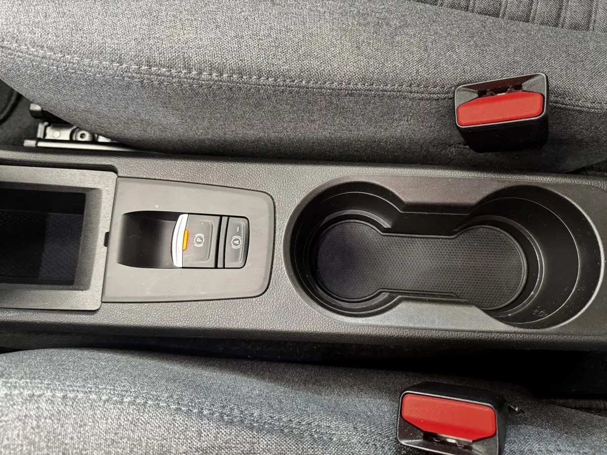 Gros plan sur la console centrale noire avec porte-gobelets et bouton de frein à main électrique de la Renault ZOE blanche.