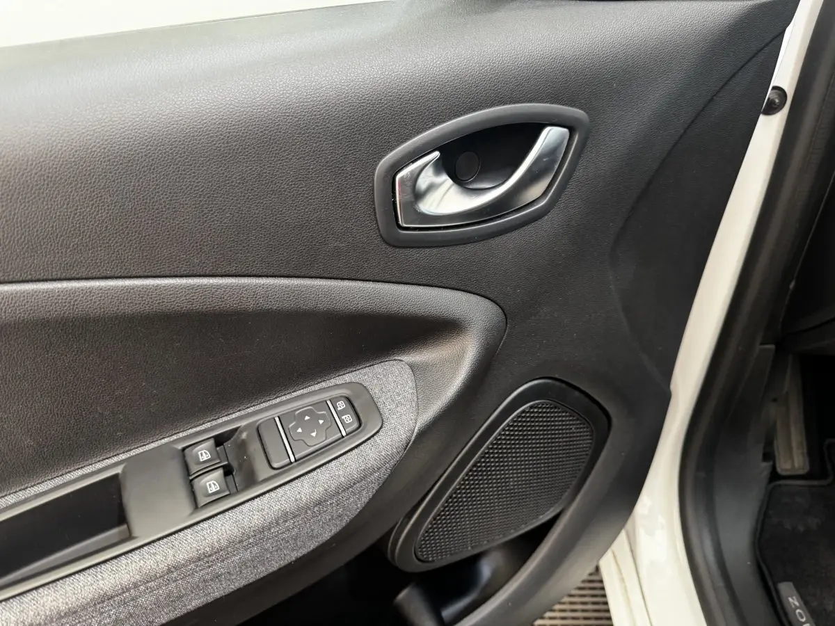 Vue rapprochée de la porte avant gauche blanche d’une Renault ZOE Iconic R135 avec commandes de vitres et poignée intérieure chromée.