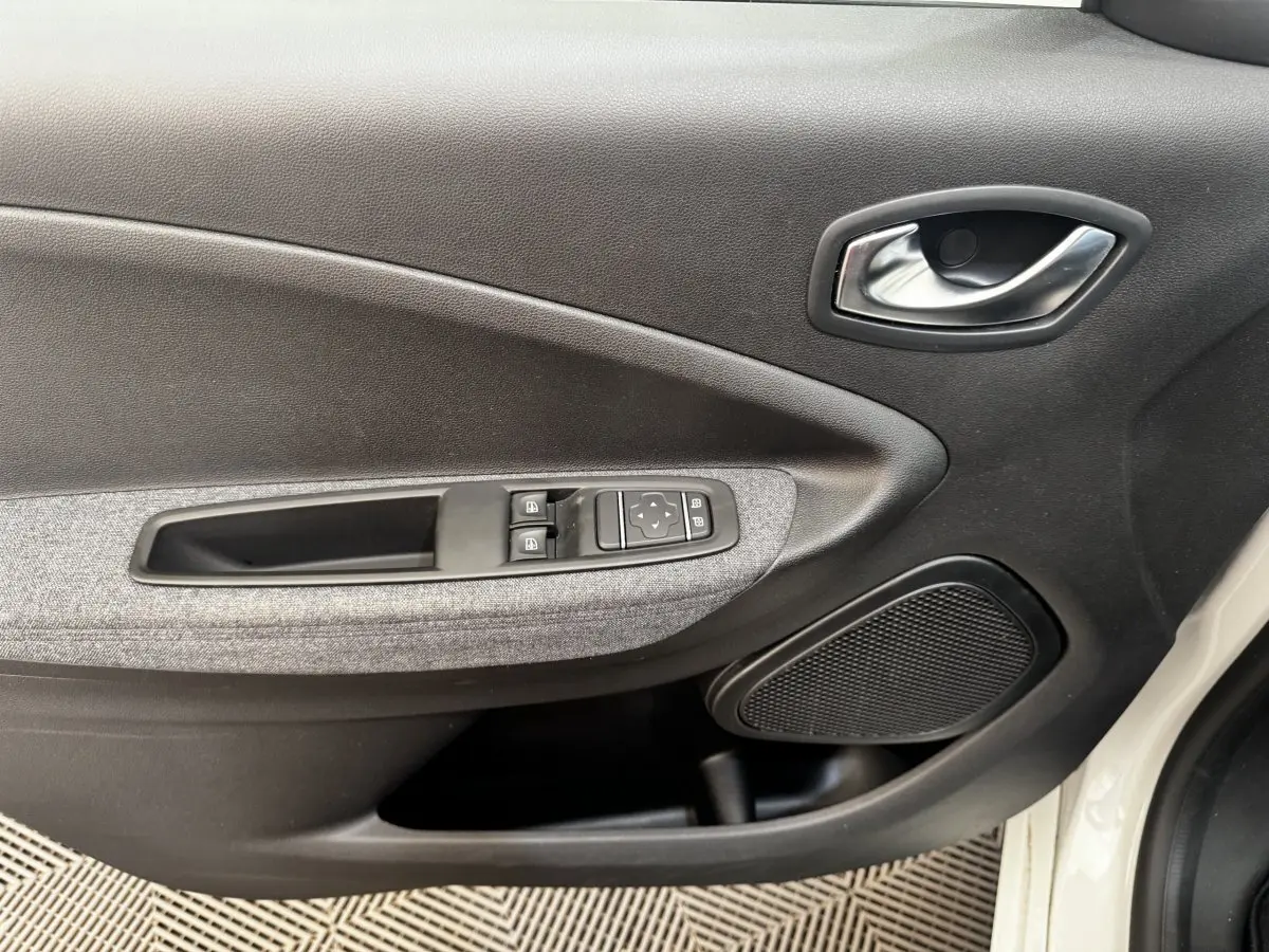 Détail de la porte avant gauche blanche d’une Renault ZOE Iconic R135 avec commandes de vitres et haut-parleur intégré.