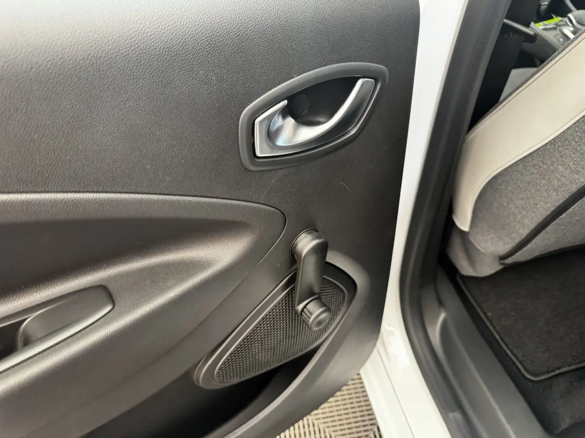 Détail de la porte arrière droite intérieure noire d'une Renault ZOE blanche, avec manivelle de vitre manuelle visible.