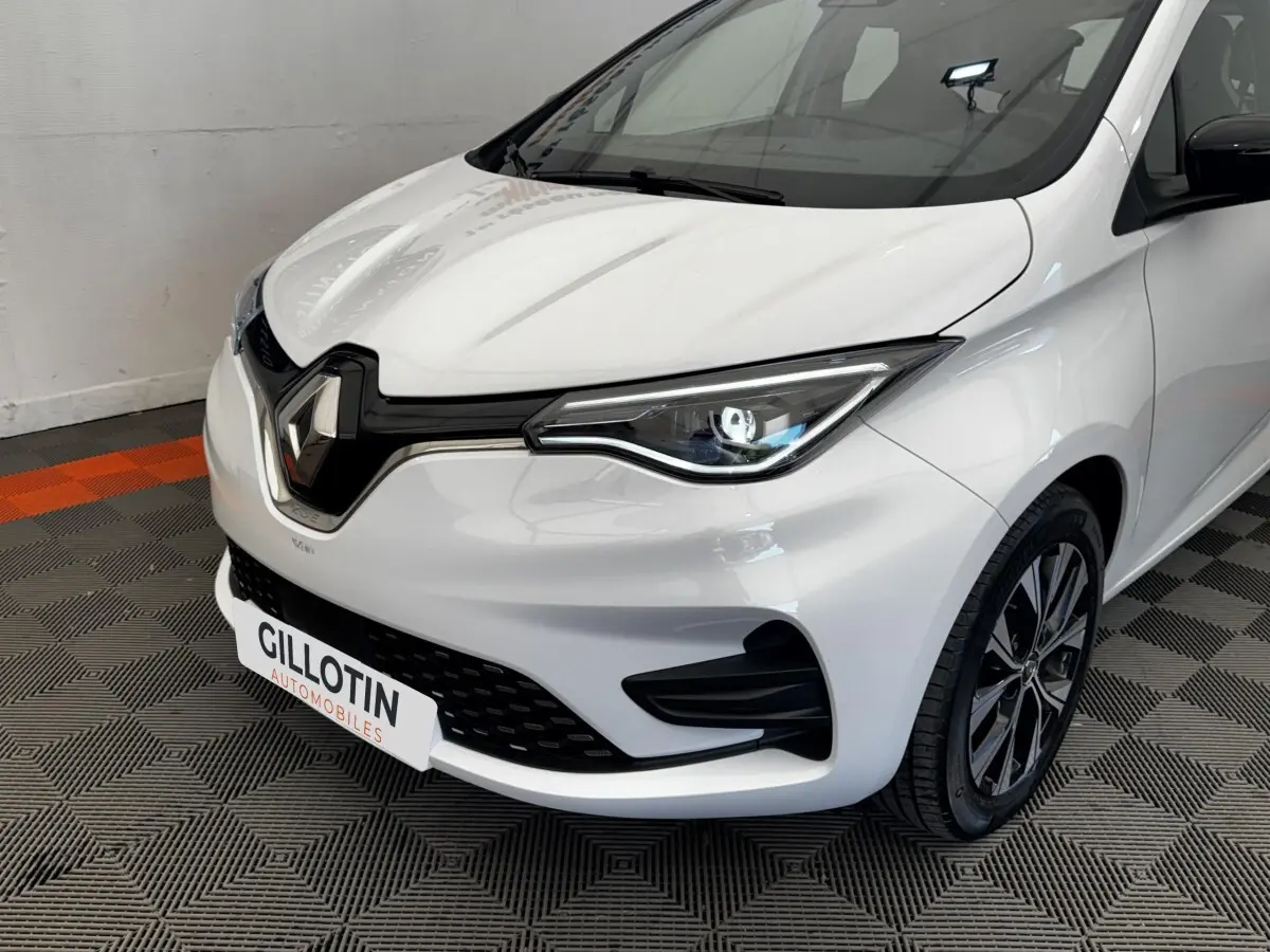 Vue 3/4 avant droit d'une Renault ZOE Iconic R135 blanche, avec phares LED et calandre noire brillante.