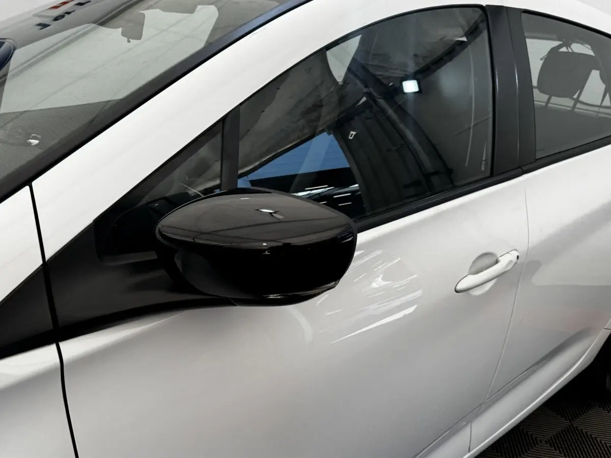 Vue rapprochée du côté gauche d'une Renault ZOE blanche avec rétroviseur noir brillant et poignée de porte blanche.