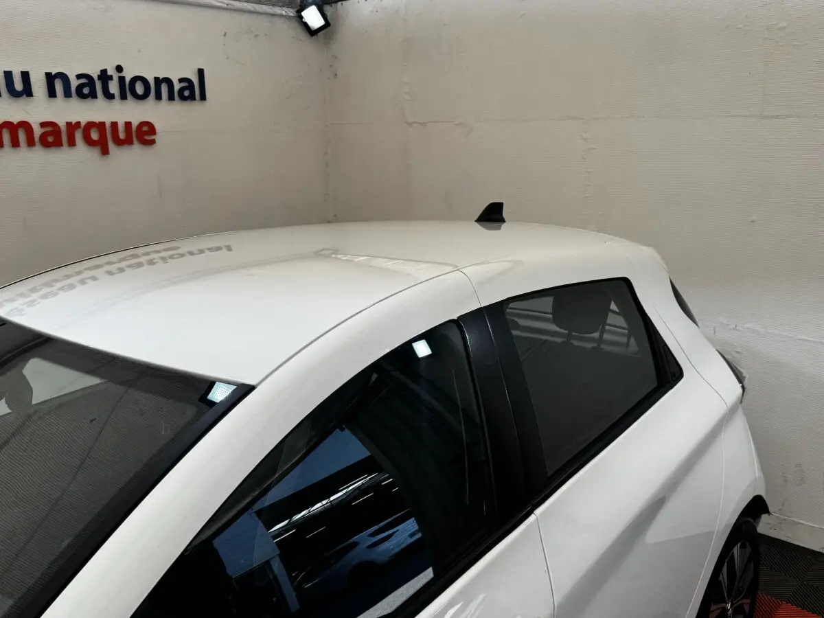 Vue 3/4 arrière droite d'une Renault ZOE Iconic R135 blanche, avec vitres teintées et antenne requin sur le toit.