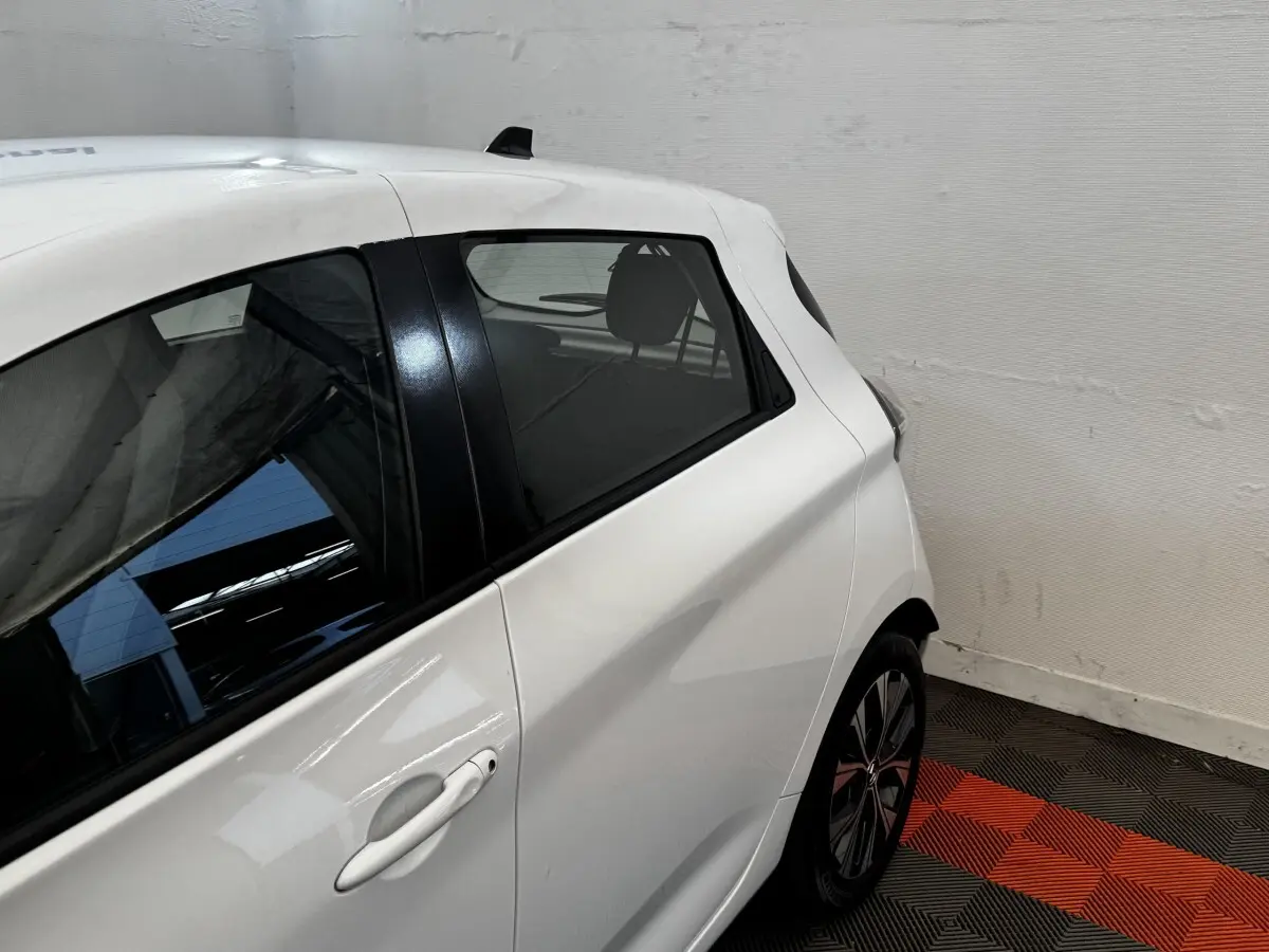Vue côté gauche arrière d'une Renault ZOE blanche, mettant en valeur la poignée de porte et la jante au design moderne.