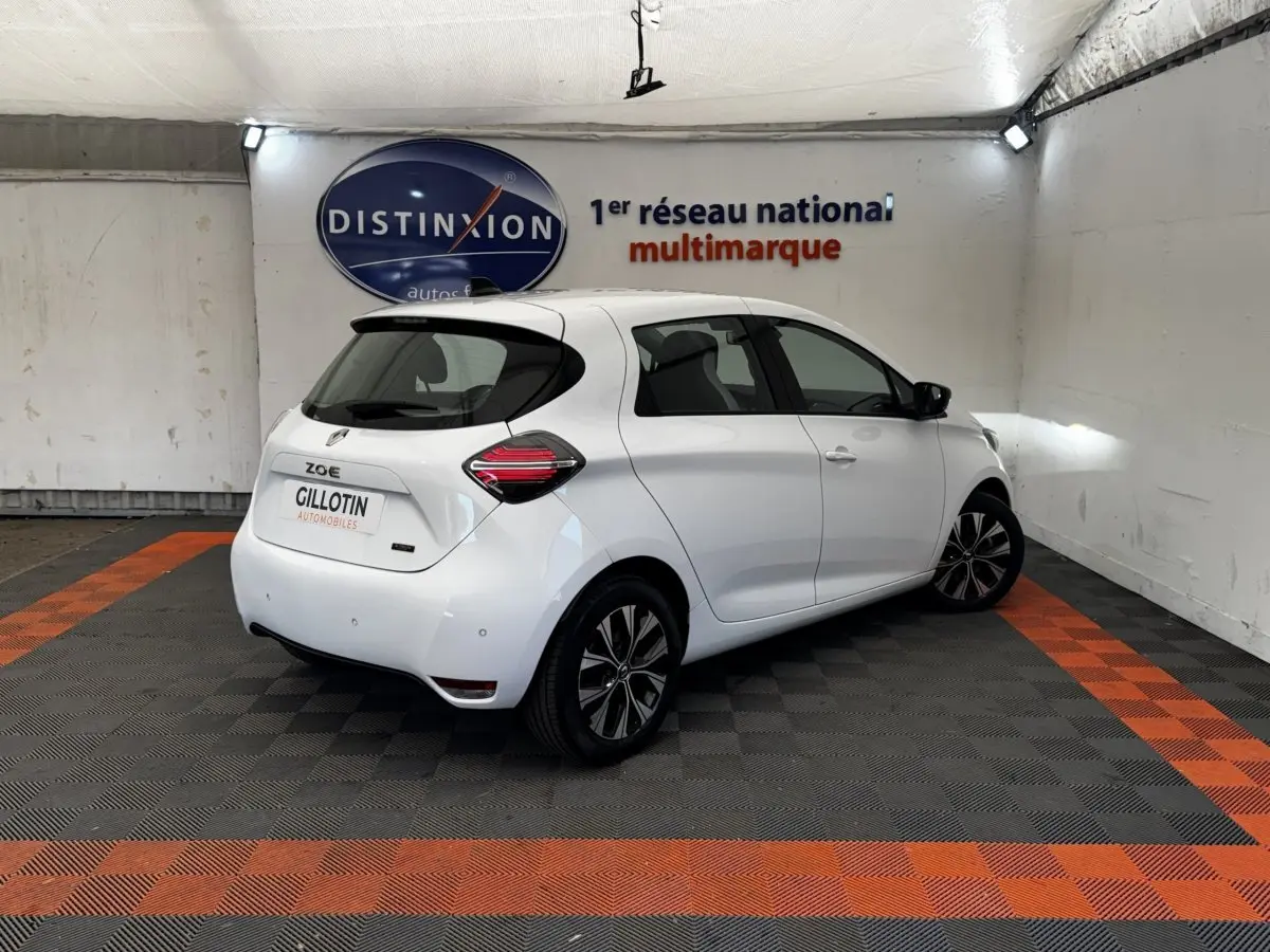 Vue 3/4 arrière droite d'une Renault ZOE blanche électrique avec feux arrière LED et jantes noires stylisées.