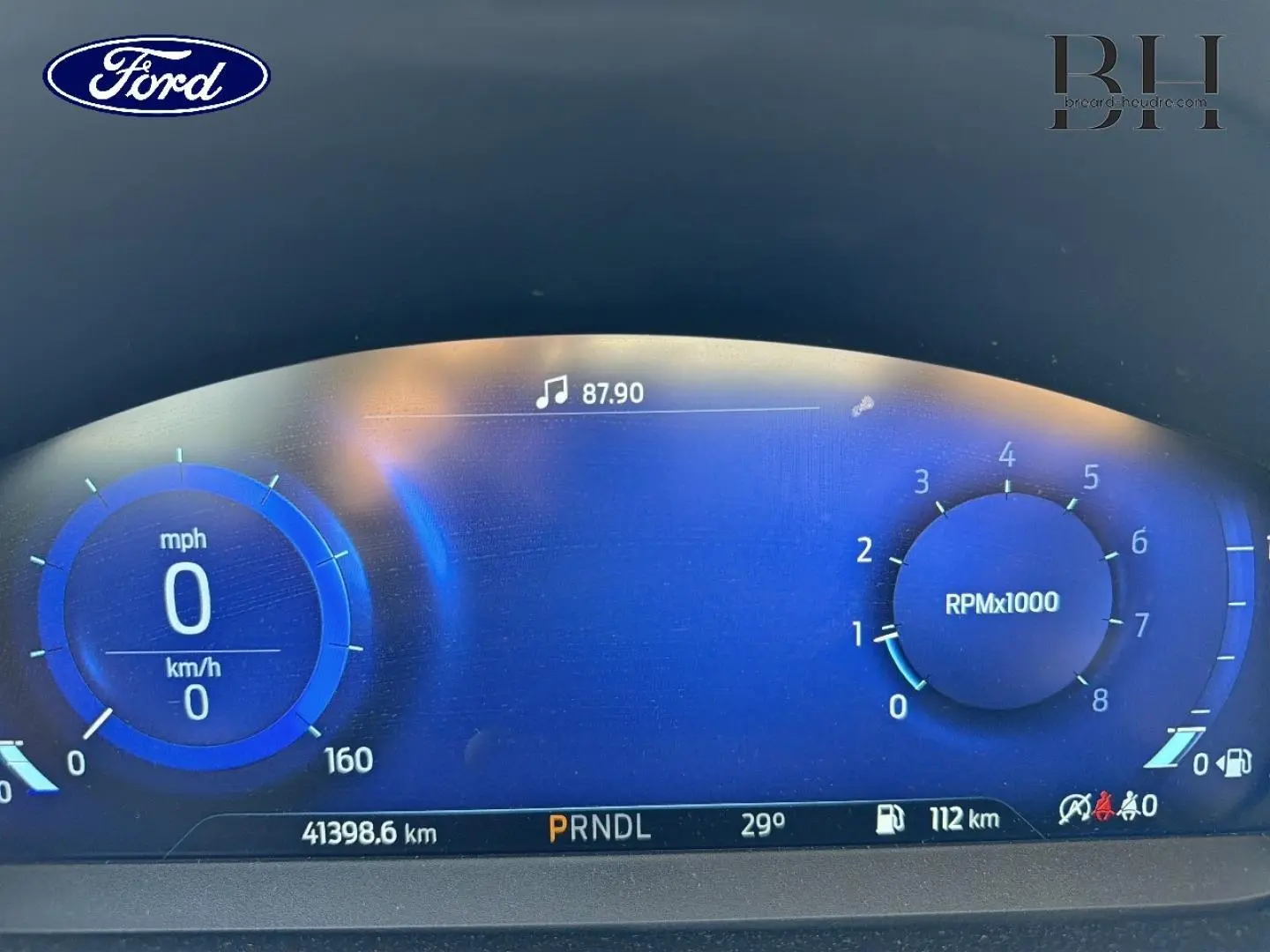 Tableau de bord numérique de Ford Focus 2023 affichant vitesse, compte-tours, température et autonomie, éclairage bleu.