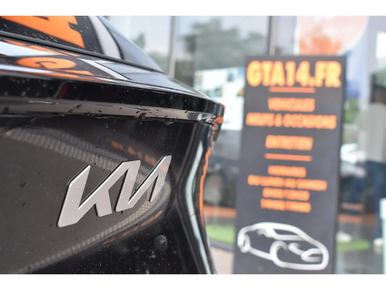 Gros plan sur l'arrière noir brillant du Kia Sportage 2026 avec logo KIA et reflet d'enseigne floue en arrière-plan.