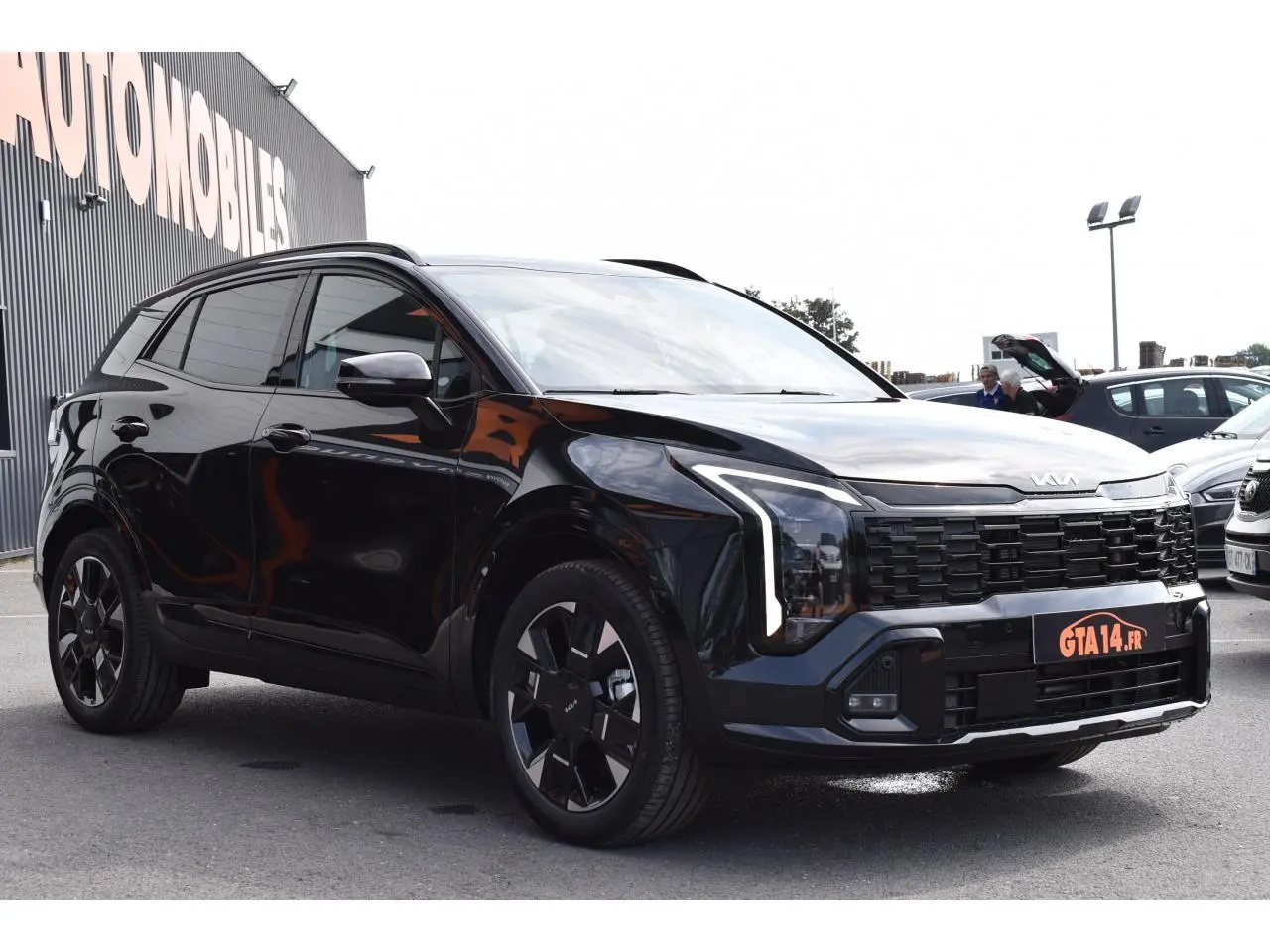 KIA SPORTAGE Hybride noir en vue 3/4 avant droit, avec calandre imposante et jantes noires distinctives.
