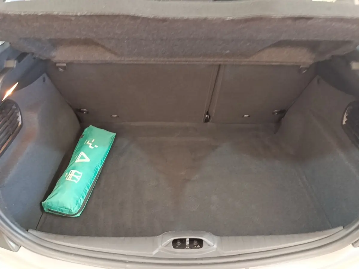 Coffre ouvert de Peugeot 208 gris clair, vue de dessus montrant un kit de sécurité vert à gauche.