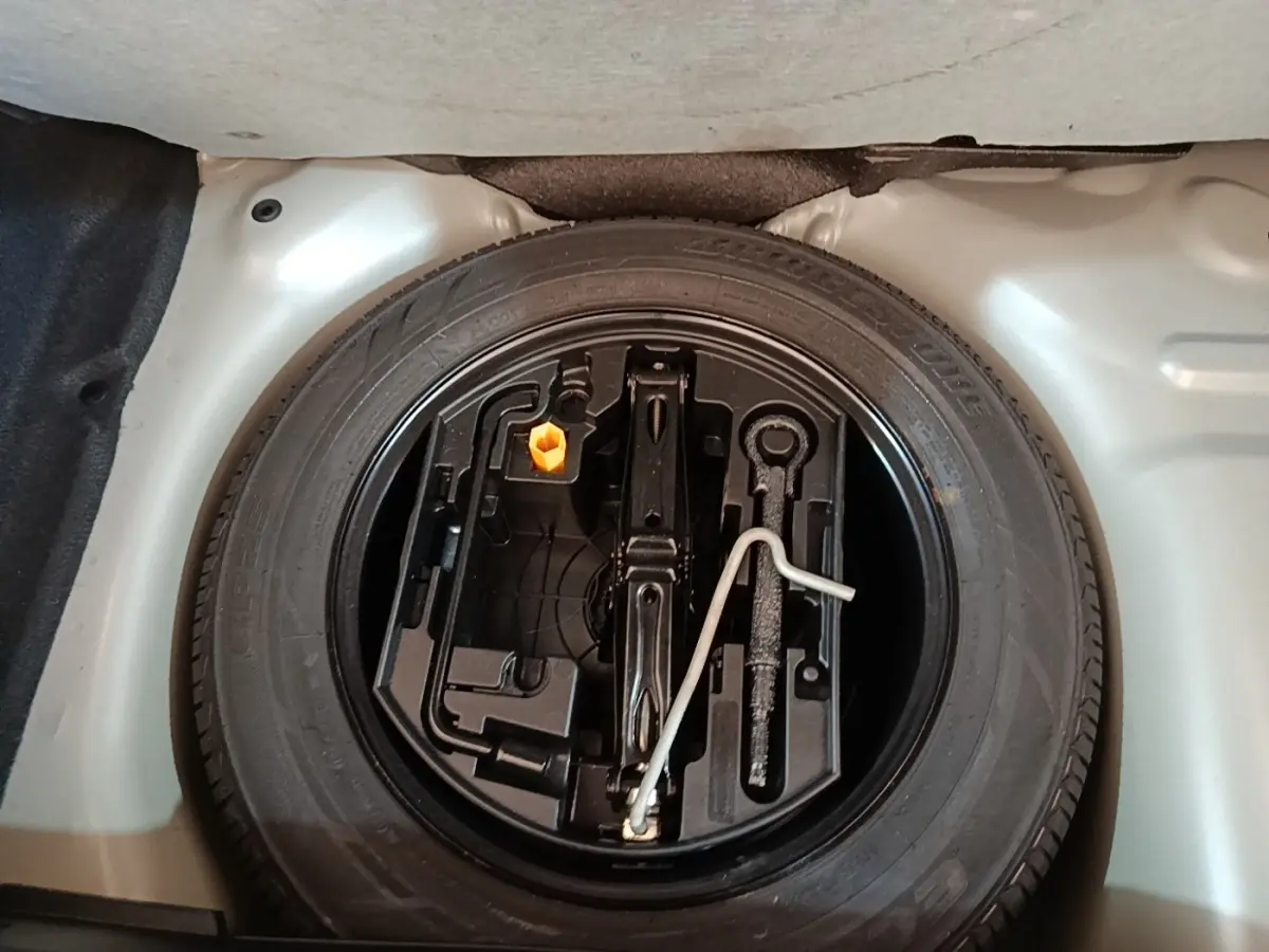 Roue de secours et outillage dans le coffre d'une Peugeot 208 gris clair, vue plongeante sur l'espace rangement.