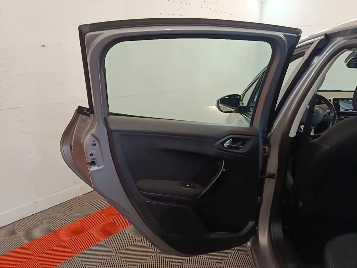 Vue intérieure sur la porte arrière gauche ouverte d'une Peugeot 208 gris clair, avec intérieur noir visible.