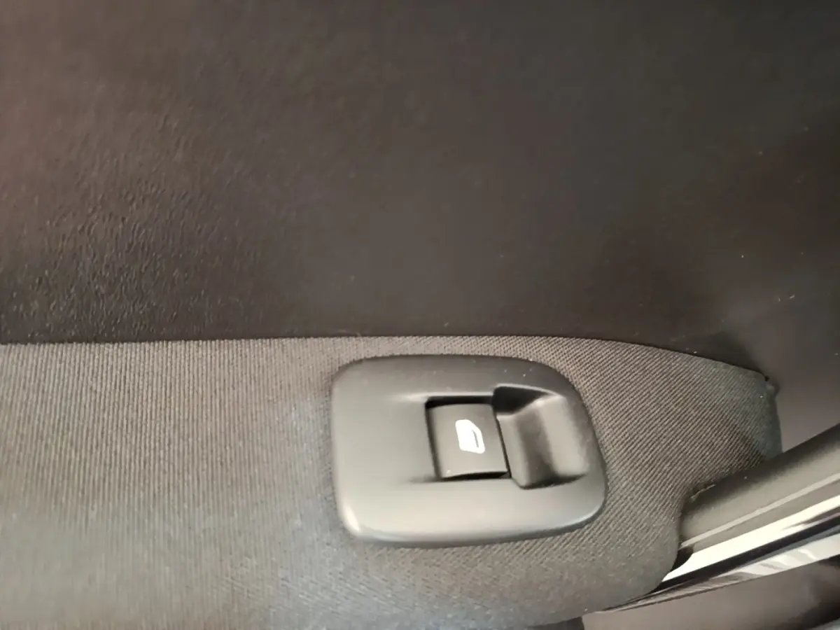 Gros plan sur le bouton de commande de lève-vitre arrière droite d’une Peugeot 208 gris clair Puretech 82 Allure.
