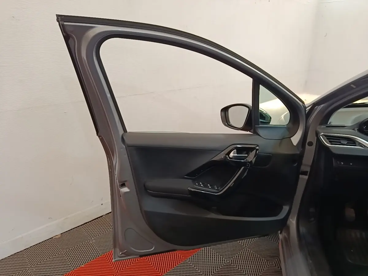 Vue intérieure de la porte avant gauche ouverte d'une Peugeot 208 gris clair, avec garniture noire et commandes électriques.