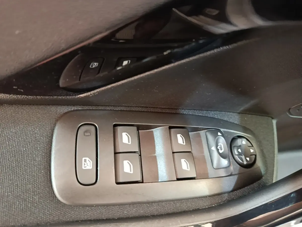 Gros plan sur les commandes de lève-vitres et rétroviseurs côté conducteur d'une Peugeot 208 gris clair.