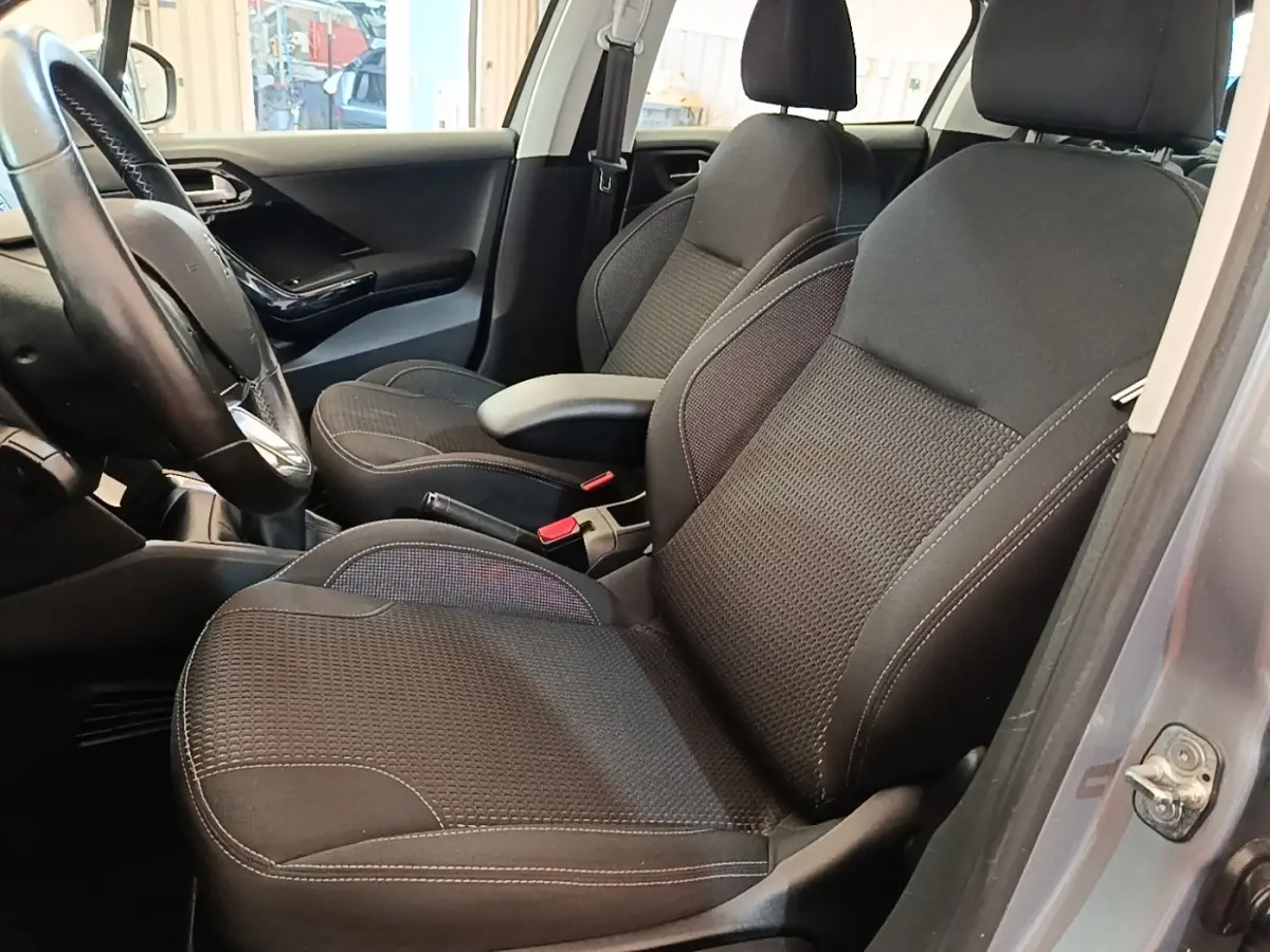Vue intérieure côté conducteur de la Peugeot 208 gris clair, sièges noirs avec coutures blanches et volant cuir.