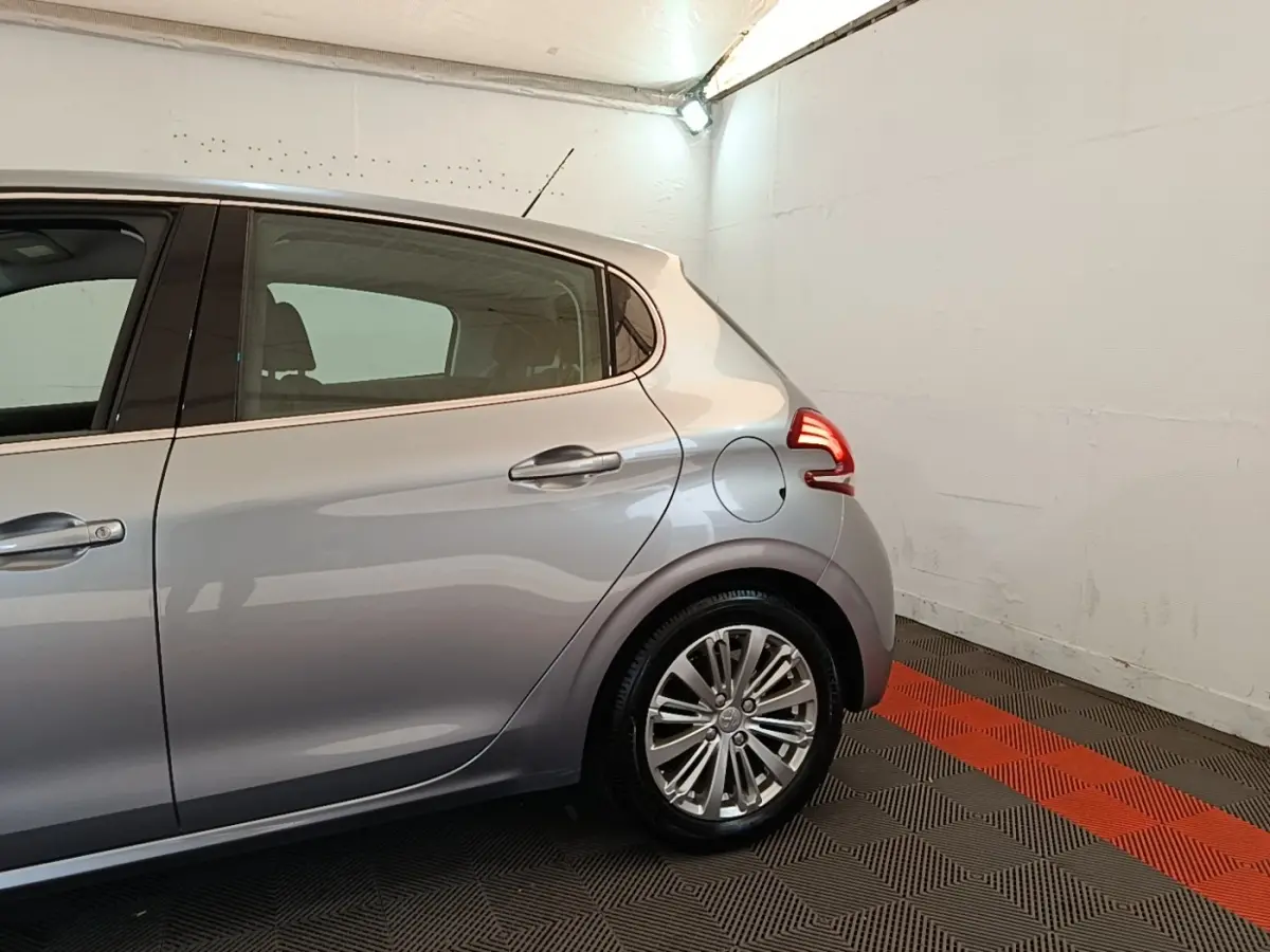 Vue latérale droite sur l'arrière d'une Peugeot 208 gris clair, avec feux arrière allumés dans un garage.