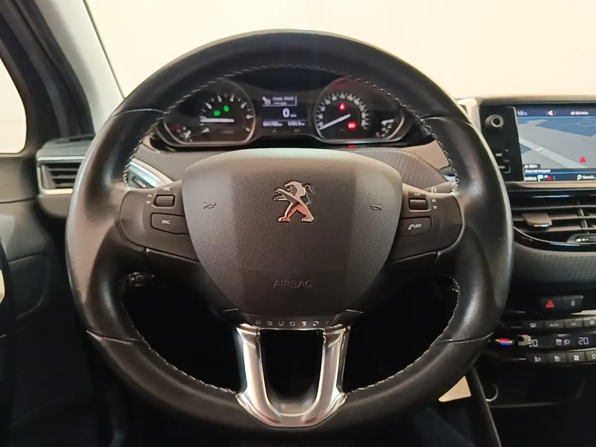 Vue rapprochée du volant cuir noir de la Peugeot 208 Puretech 82 Allure avec tableau de bord et écran tactile visible.