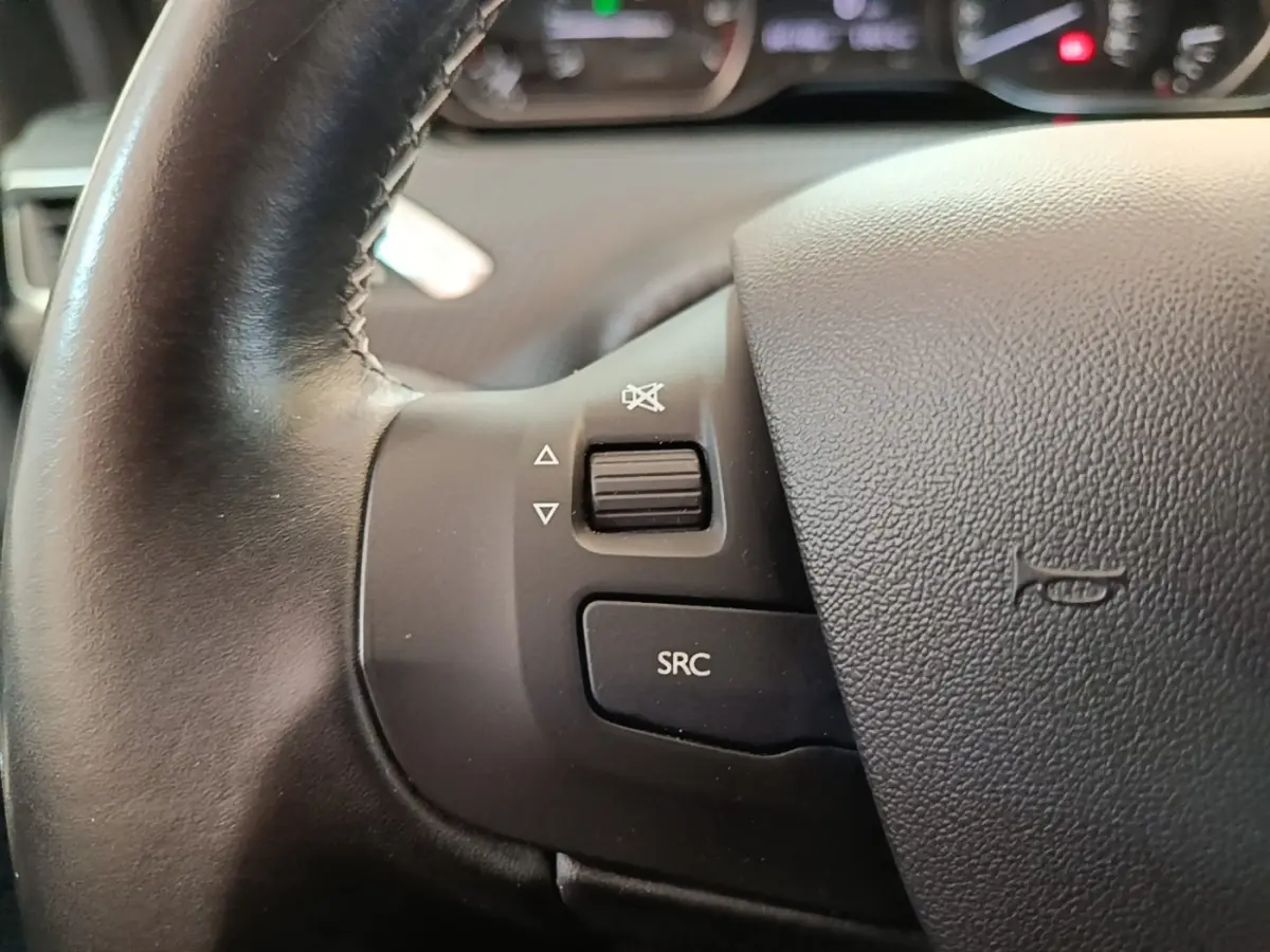Gros plan sur le volant cuir noir de la Peugeot 208 Puretech 82 Allure, avec commandes audio intégrées.