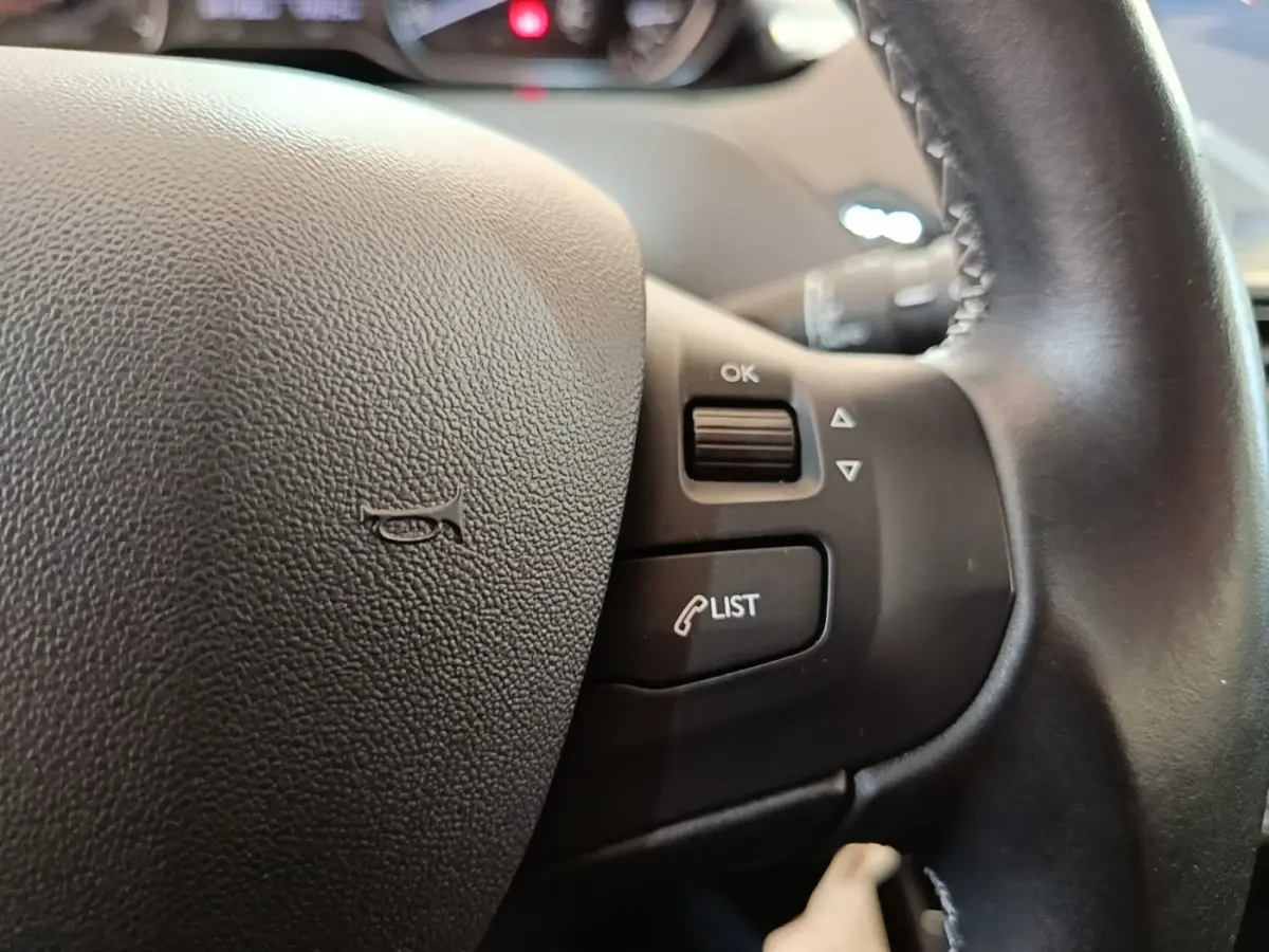 Gros plan sur le volant en cuir noir du Peugeot 208 Puretech 82 Allure avec commandes intégrées côté droit.