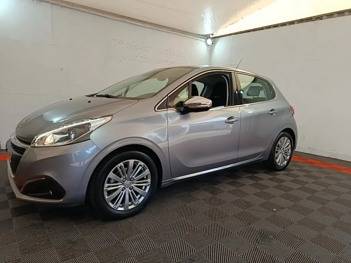 Peugeot 208 gris clair vue 3/4 avant droit en intérieur avec jantes alliage et rétroviseurs chromés.