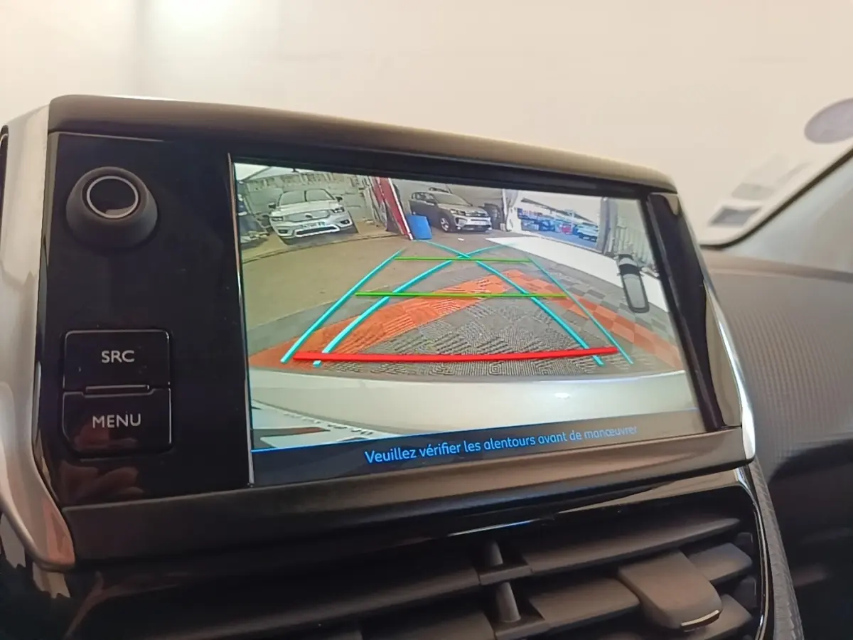 Écran tactile intérieur montrant la caméra de recul d'une Peugeot 208 gris clair, avec lignes de guidage colorées.