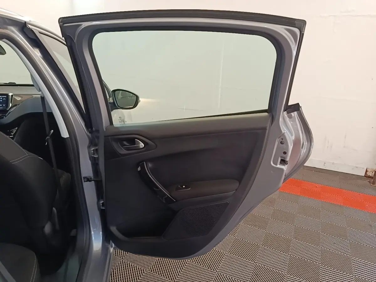 Vue intérieure côté gauche de la porte arrière ouverte d'une Peugeot 208 gris clair, montrant la garniture noire.