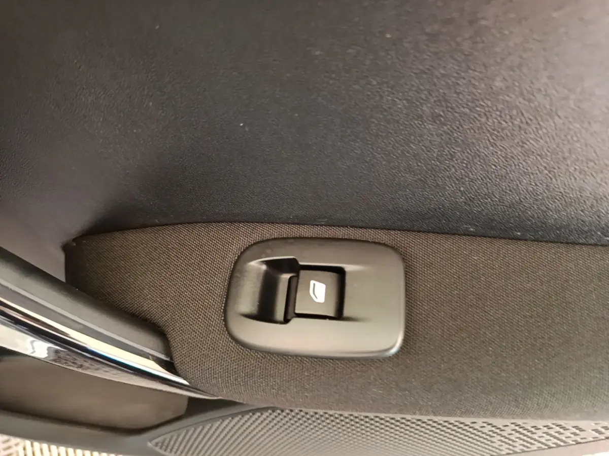Détail du bouton de commande de lève-vitre sur la porte intérieure tissu d'une Peugeot 208 gris clair.