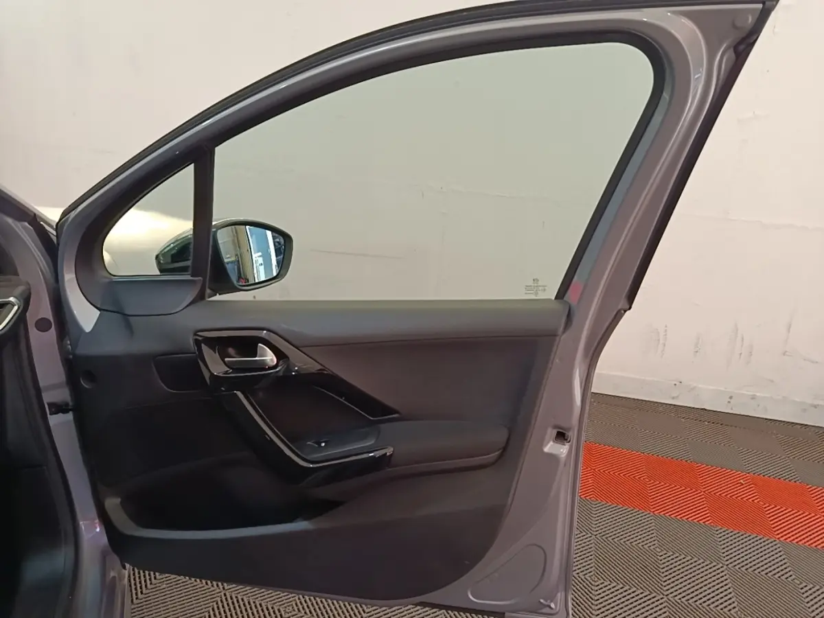 Vue intérieure de la porte avant gauche gris clair d'une Peugeot 208 Puretech 82 Allure avec poignée noire brillante.