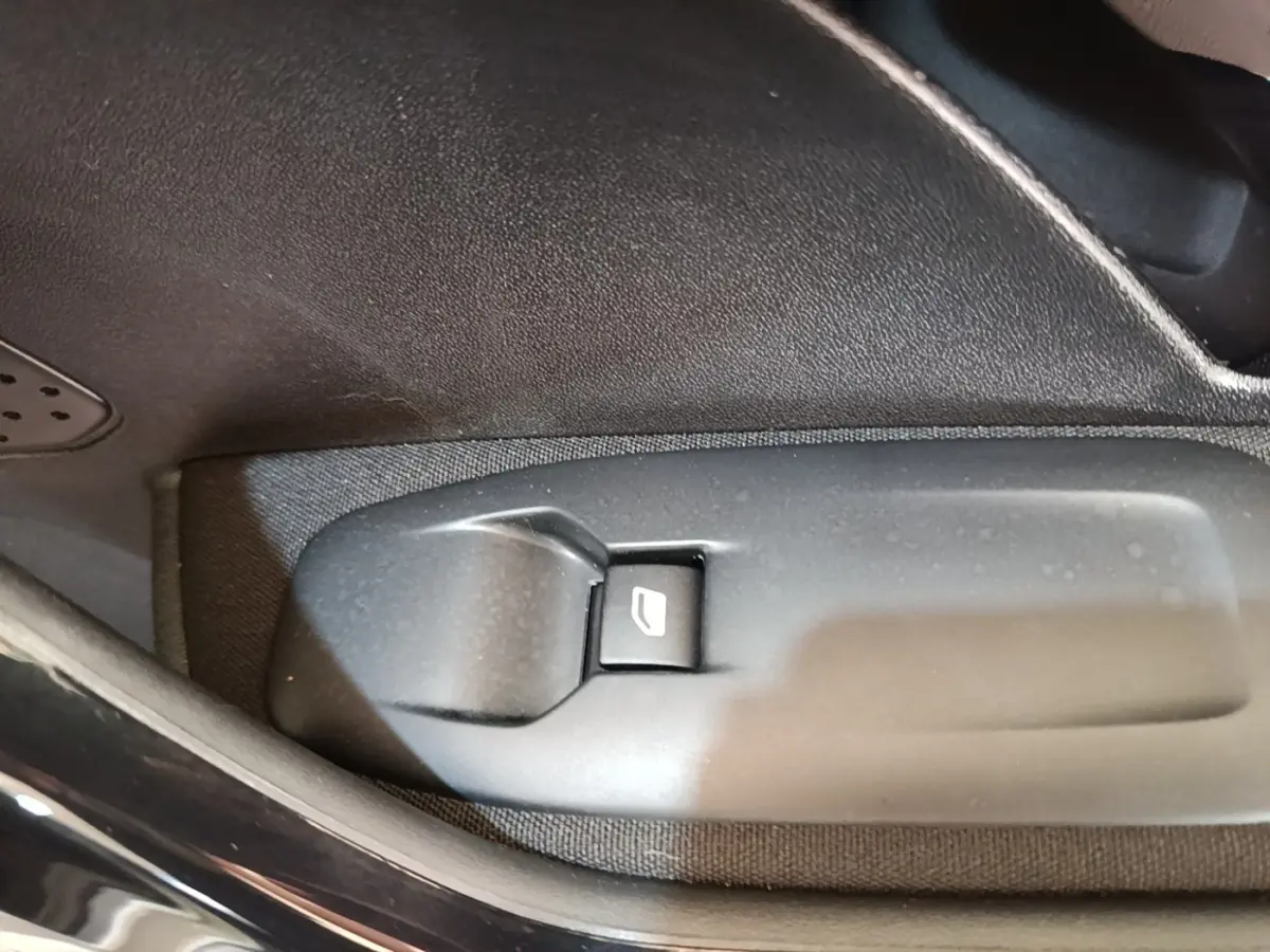 Gros plan sur le bouton de commande de lève-vitre côté conducteur dans l'habitacle d'une Peugeot 208 gris clair.