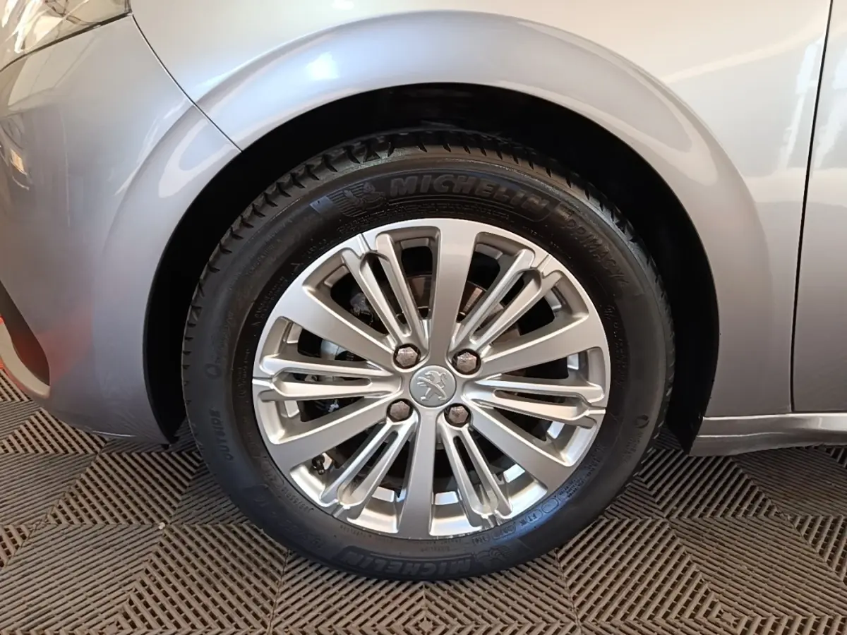 Gros plan sur la roue avant gauche gris clair d'une Peugeot 208 Puretech 82 Allure avec jante alliage.