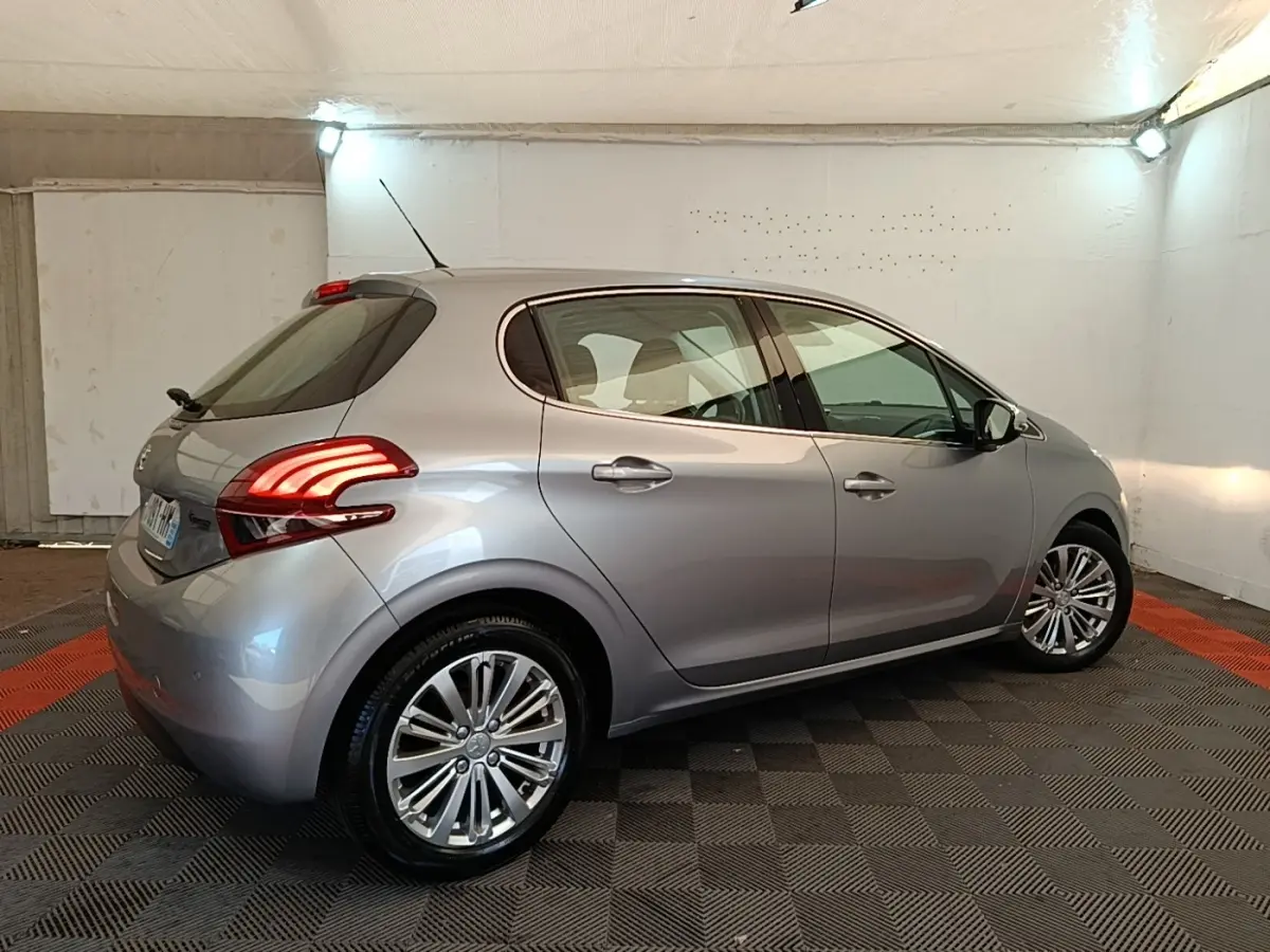 Peugeot 208 Puretech 82 Allure gris clair vue 3/4 arrière droit en intérieur avec feux arrière LED allumés.
