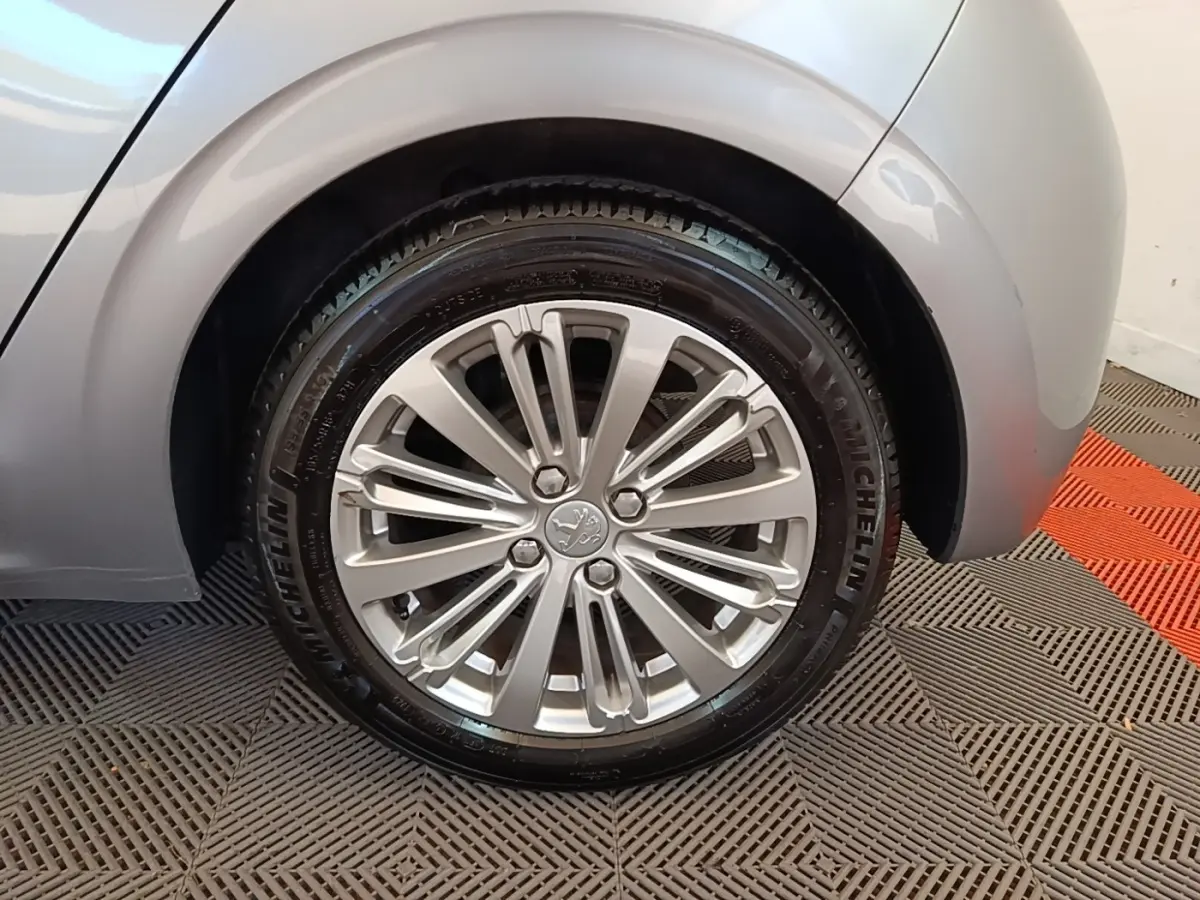 Gros plan sur la roue arrière droite grise claire d'une Peugeot 208 Puretech 82 Allure avec jante alliage multibranches.
