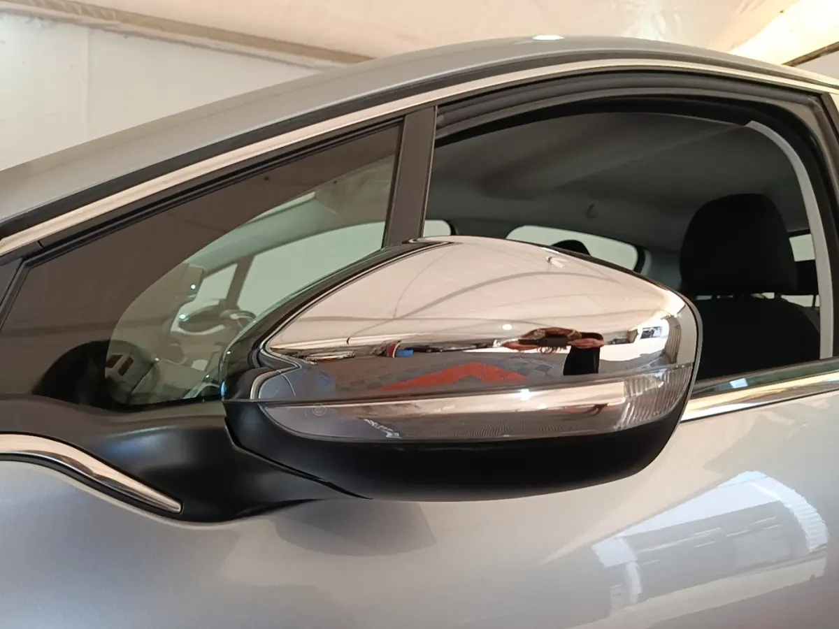 Rétroviseur chromé côté conducteur d’une Peugeot 208 gris clair, vue rapprochée sur la portière avant.