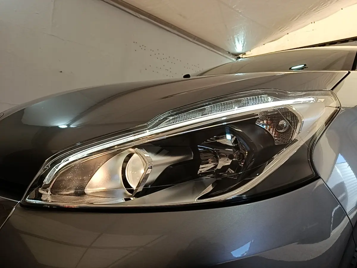 Gros plan sur le phare avant droit de la Peugeot 208 Puretech 82 Allure gris clair, avec reflet lumineux.