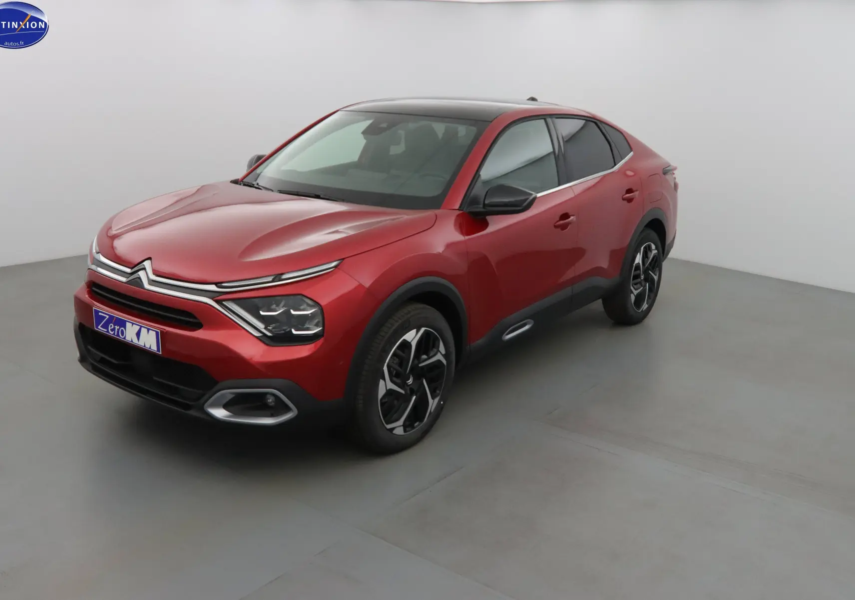 Citroën C4 X rouge Elixir métal vue 3/4 avant droit, avec toit noir et jantes bicolores distinctives.