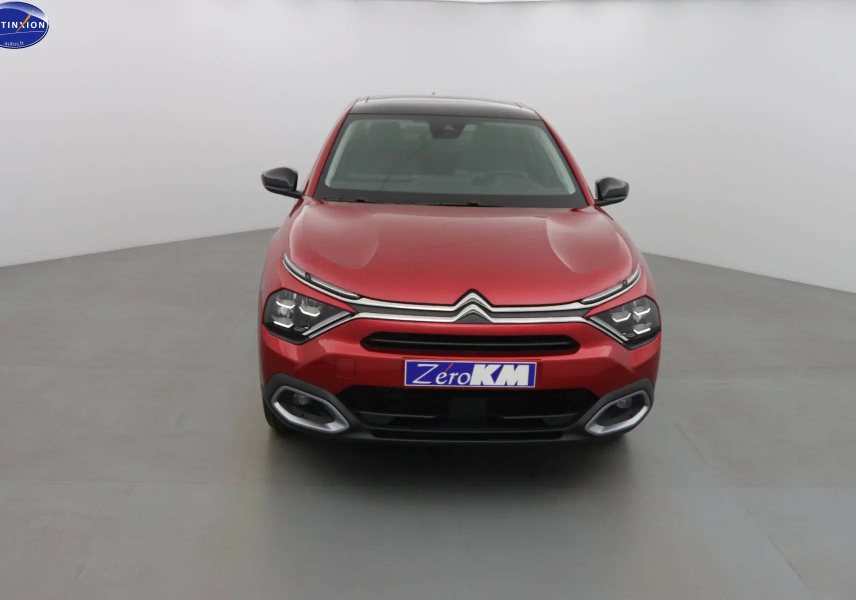 Vue frontale d'une Citroën C4 X rouge Elixir métal avec calandre chromée et feux LED distinctifs allumés.