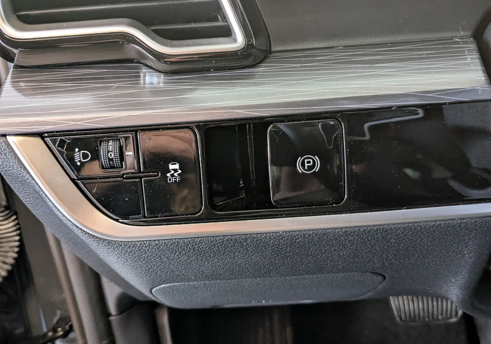 Gros plan sur les commandes de la console centrale du Kia Sportage gris eclipse MY25, avec bouton de frein à main électronique et régulateur de phare.