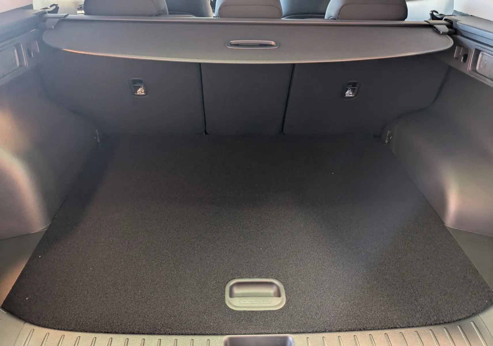 Coffre spacieux et propre du Kia Sportage MY25 gris eclipse, vu de l'arrière avec cache-bagages en place.
