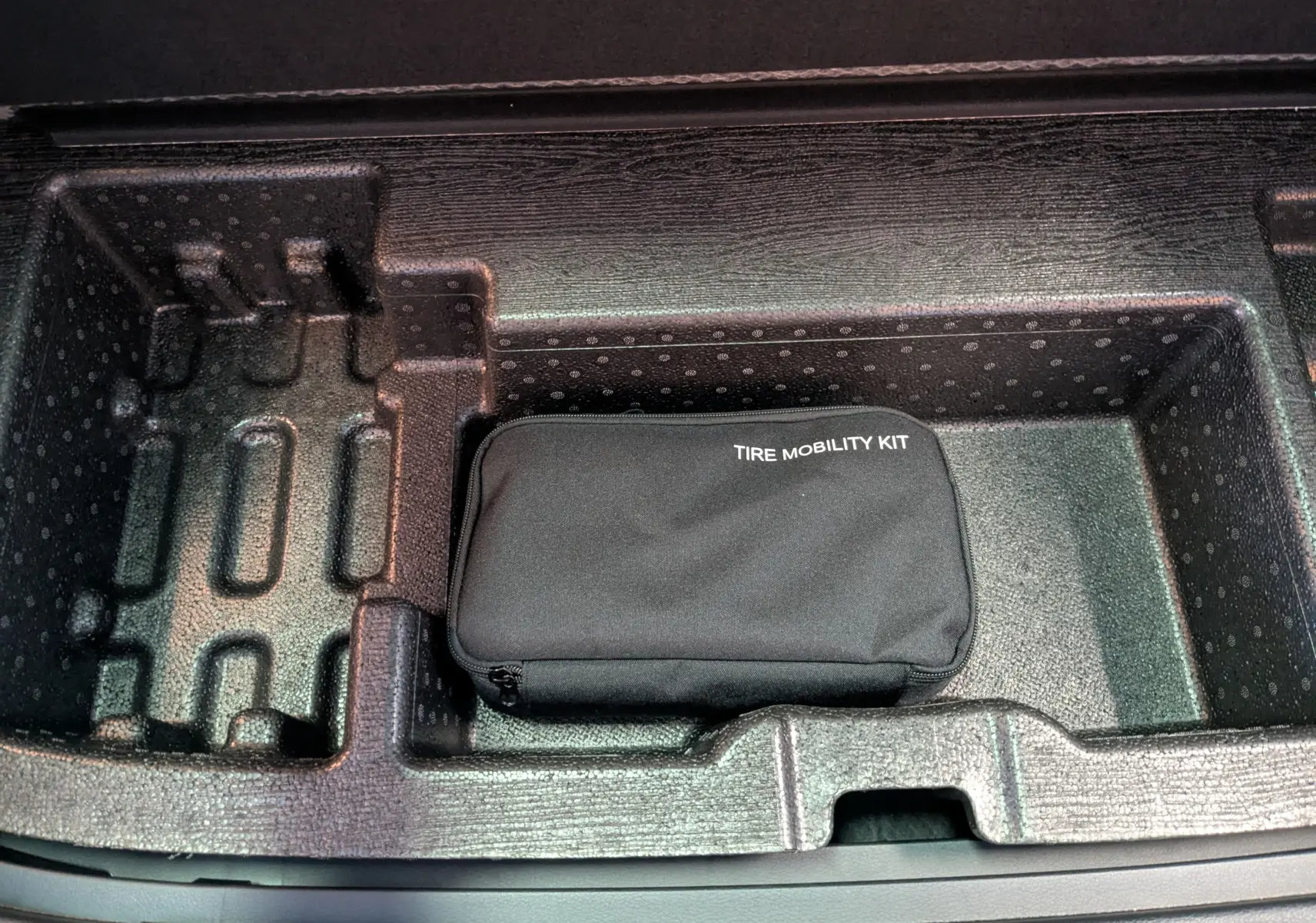 Vue intérieure du coffre du KIA SPORTAGE gris eclipse MY25 avec kit de mobilité pneus rangé dans compartiment en mousse noire.