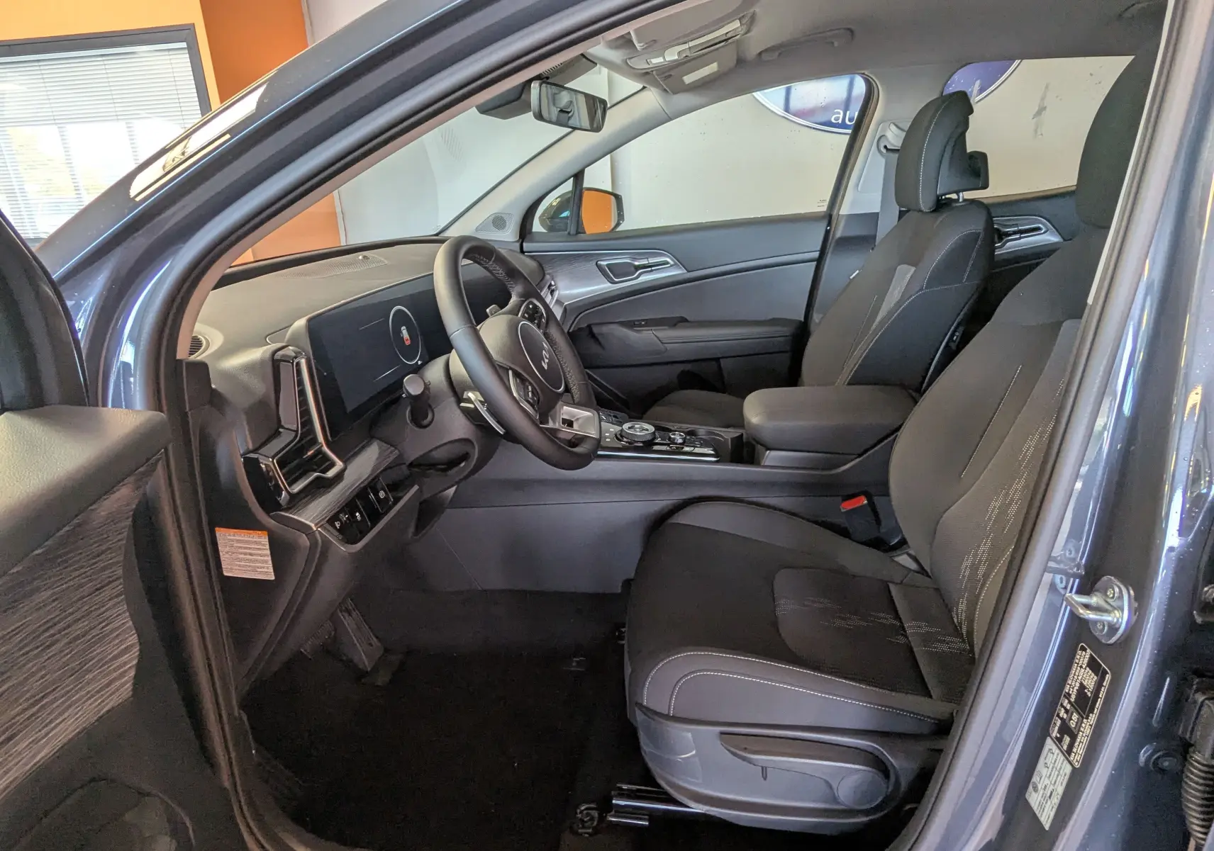 Intérieur avant du Kia Sportage gris eclipse MY25, sièges tissu gris, tableau de bord moderne avec écran tactile 12,3 pouces.