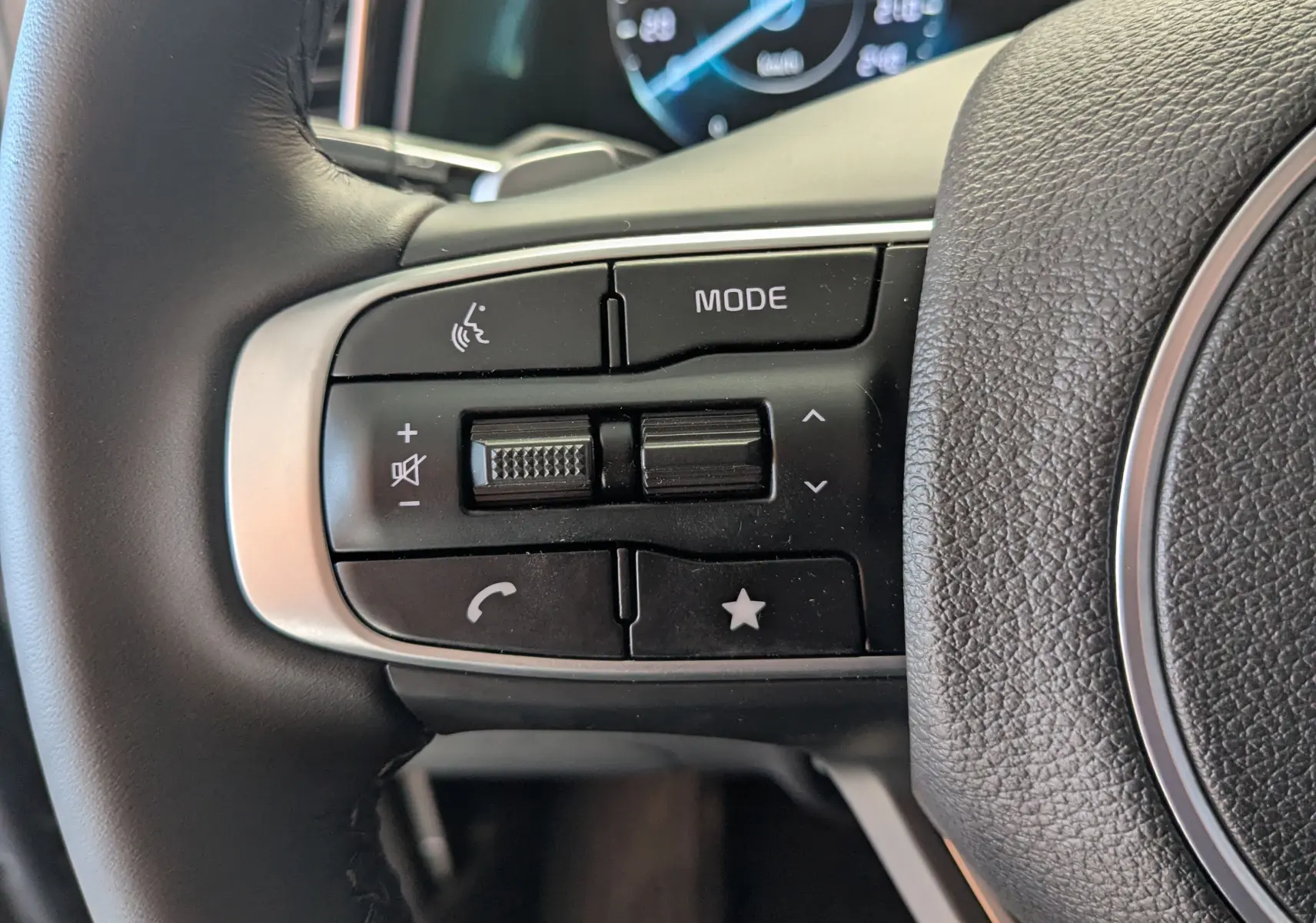 Gros plan sur les commandes gauche du volant en cuir noir du Kia Sportage gris eclipse MY25, avec boutons multifonctions.