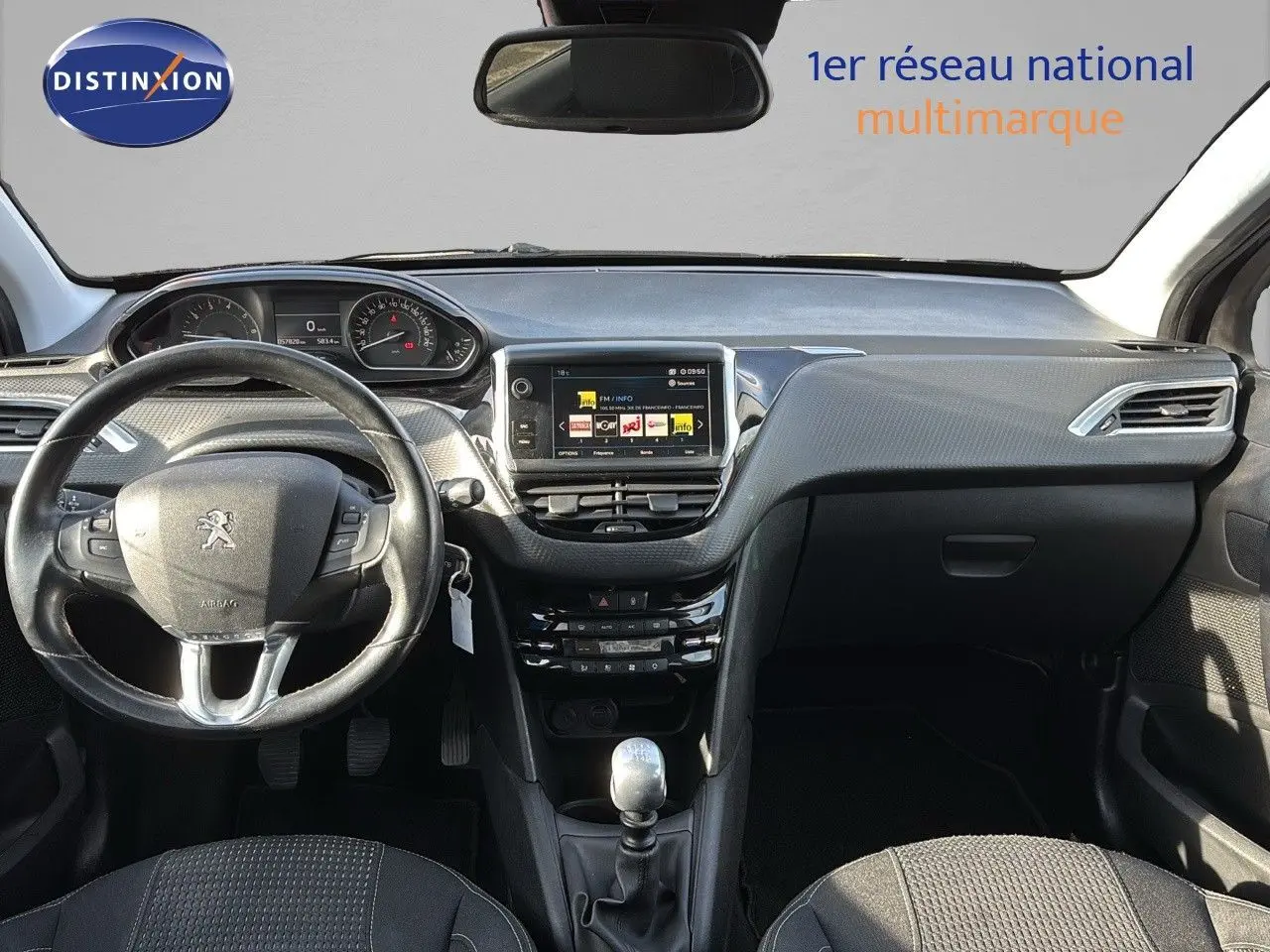 Intérieur noir de la Peugeot 208 2019, vue frontale du tableau de bord avec volant, écran tactile et levier de vitesse manuel.