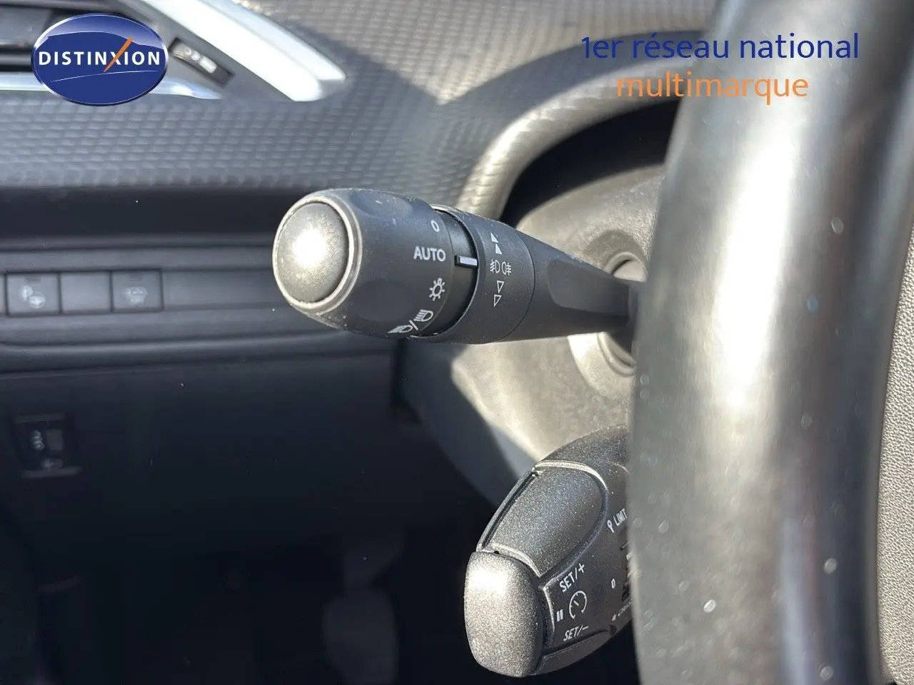 Gros plan sur les commandes au volant d'une Peugeot 208 noire, montrant les leviers de clignotants et régulateur de vitesse.