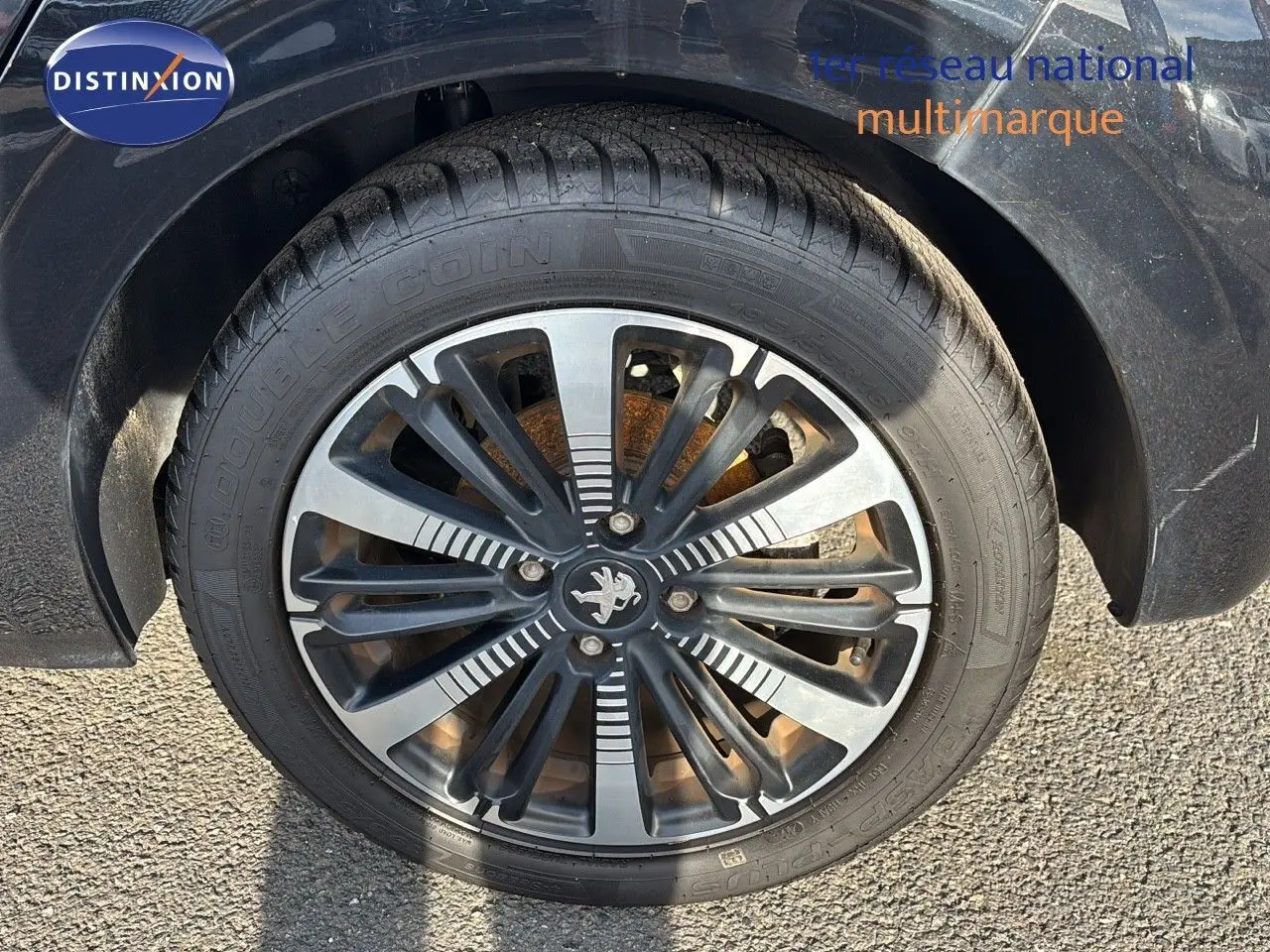 Gros plan sur la roue avant gauche d'une Peugeot 208 noire perle métal avec jante alliage distinctive.