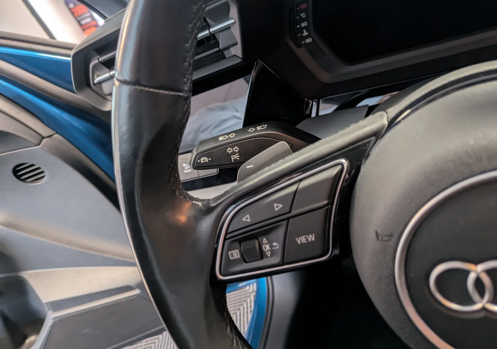 Gros plan sur le volant et la commande multifonction d'une Audi A3 Sportback bleu Atollblau, côté conducteur ouvert.