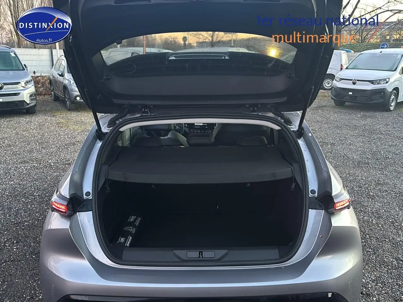 Vue arrière ouverte sur coffre spacieux d'une Peugeot 308 1.2 hybrid 145 allure gris artense avec feux arrière LED allumés.