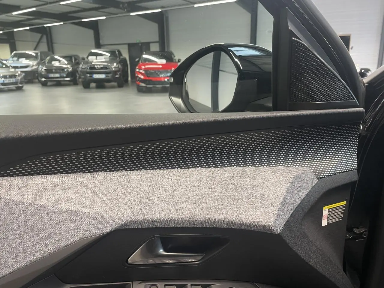 Vue intérieure côté gauche de la porte avant d’un Peugeot 3008 noir métallisé, avec tissu gris et inserts noirs laqués.